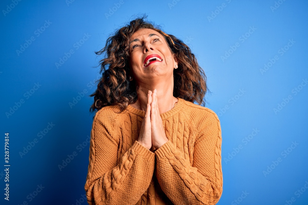 Middle age beautiful woman wearing casual yellow sweater over isolated yellow background begging and praying with hands together with hope expression on face very emotional and worried. Begging. Middle age beautiful woman wearing casual yellow sweater over isolated yellow background begging and praying with hands together with hope expression on face very emotional and worried. Begging.