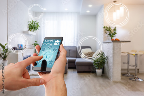 Smart home technology interface on smartphone app screen with augmented reality (AR) view of internet of things (IOT) connected objects in the apartment interior, person holding device photo