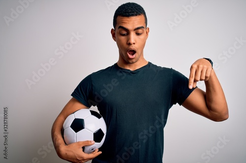 Handsome african american man playing footbal holding soccer ball over white background Pointing down with fingers showing advertisement, surprised face and open mouth