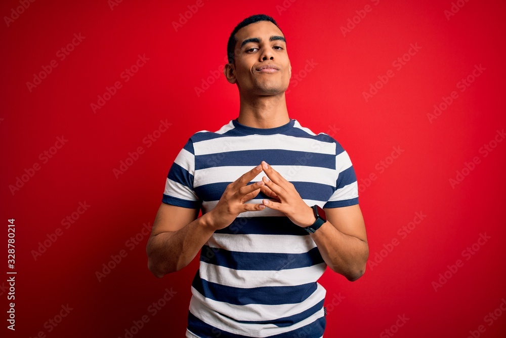 Handsome african american man wearing casual striped t-shirt standing over red background Hands together and fingers crossed smiling relaxed and cheerful. Success and optimistic Handsome african american man wearing casual striped t-shirt standing over red background Hands together and fingers crossed smiling relaxed and cheerful. Success and optimistic