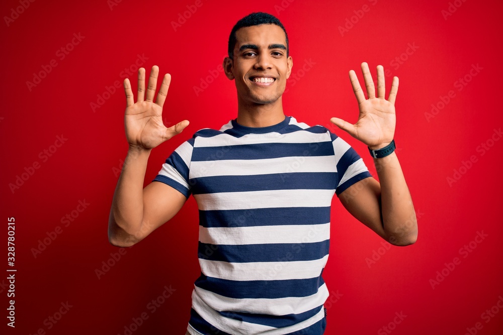Naklejka premium Handsome african american man wearing casual striped t-shirt standing over red background showing and pointing up with fingers number ten while smiling confident and happy.