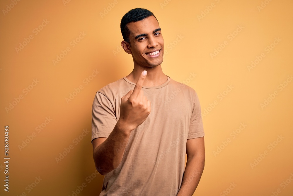 Young handsome african american man wearing casual t-shirt standing over yellow background Beckoning come here gesture with hand inviting welcoming happy and smiling Young handsome african american man wearing casual t-shirt standing over yellow background Beckoning come here gesture with hand inviting welcoming happy and smiling