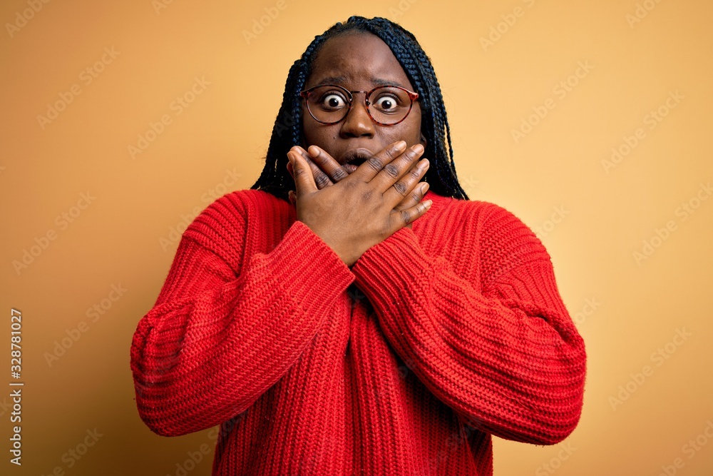 Obraz premium African american plus size woman with braids wearing casual sweater over yellow background shocked covering mouth with hands for mistake. Secret concept.