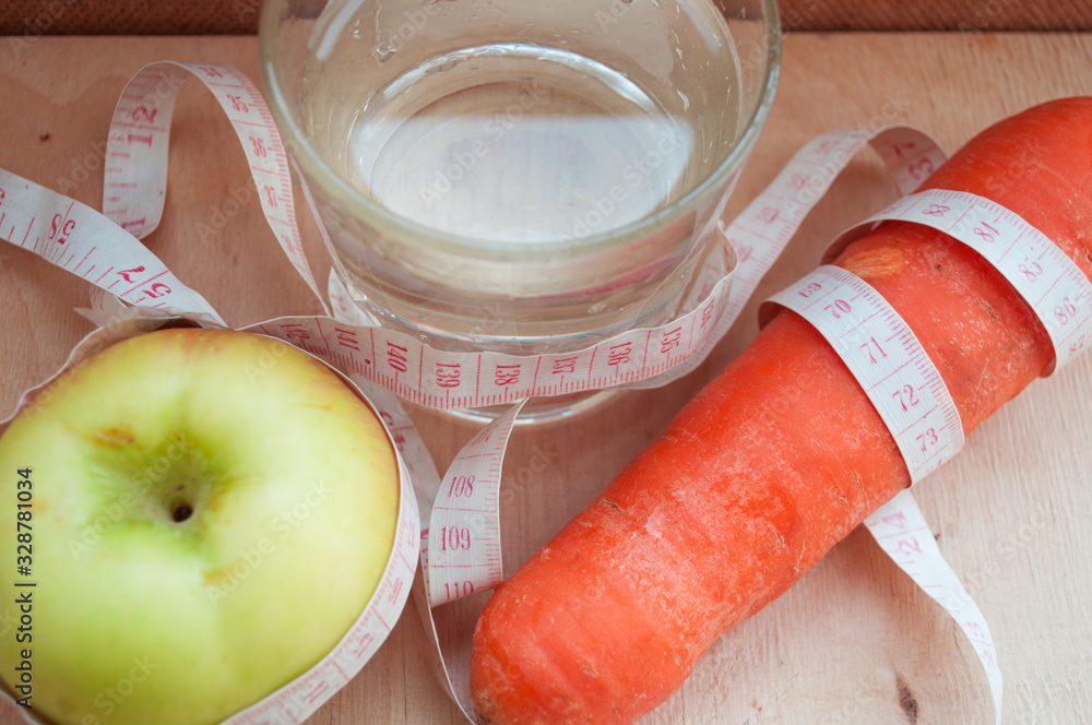 A glass of water, a carrot and an apple wrapped in tape measure. Healthy lifestyle. Lose Weight By Summer. Proper nutrition. Diet. Caring for yourself and your health. Vegetables. A glass of water, a carrot and an apple wrapped in tape measure. Healthy lifestyle. Lose Weight By Summer. Proper nutrition. Diet. Caring for yourself and your health. Vegetables.