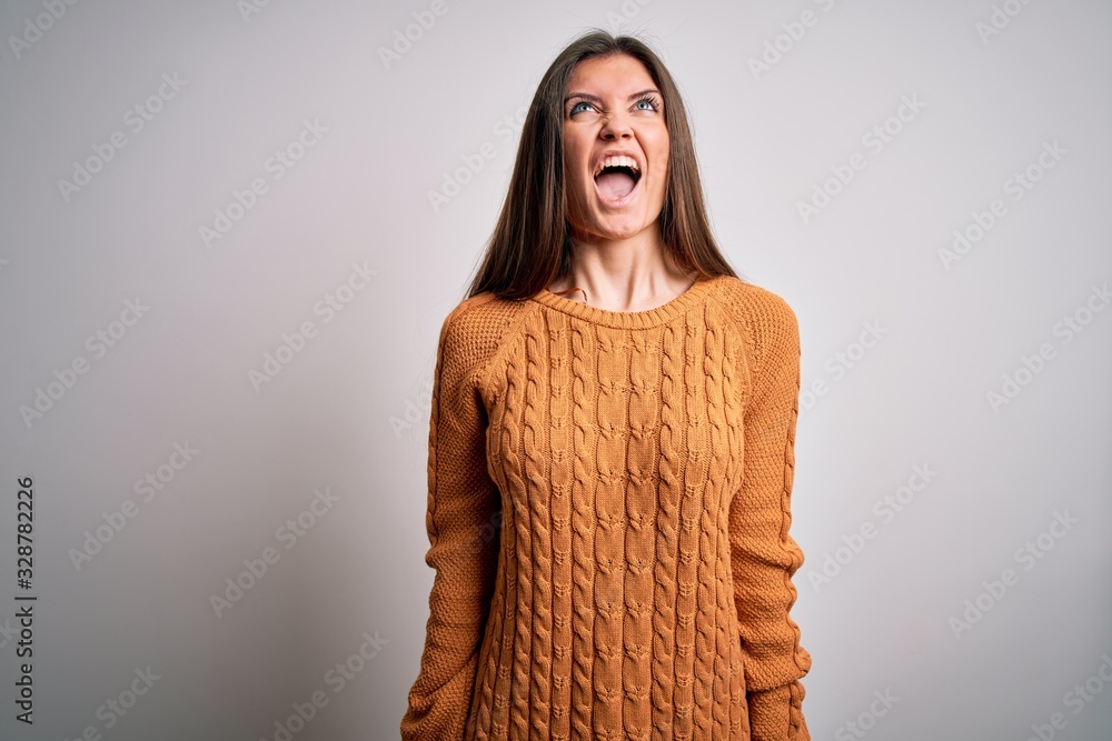 Young beautiful woman with blue eyes wearing casual sweater standing over white background angry and mad screaming frustrated and furious, shouting with anger. Rage and aggressive concept. Young beautiful woman with blue eyes wearing casual sweater standing over white background angry and mad screaming frustrated and furious, shouting with anger. Rage and aggressive concept.