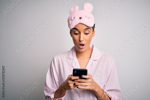Young beautiful woman wearing pajama and sleep mask having conversation using smartphone scared in shock with a surprise face, afraid and excited with fear expression © Krakenimages.com