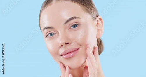 Close up of beauty woman face looking at camera, isolated on blue background. Beautiful female model with perfect clean fresh skin. Skin care treatment or cosmetic ads concept