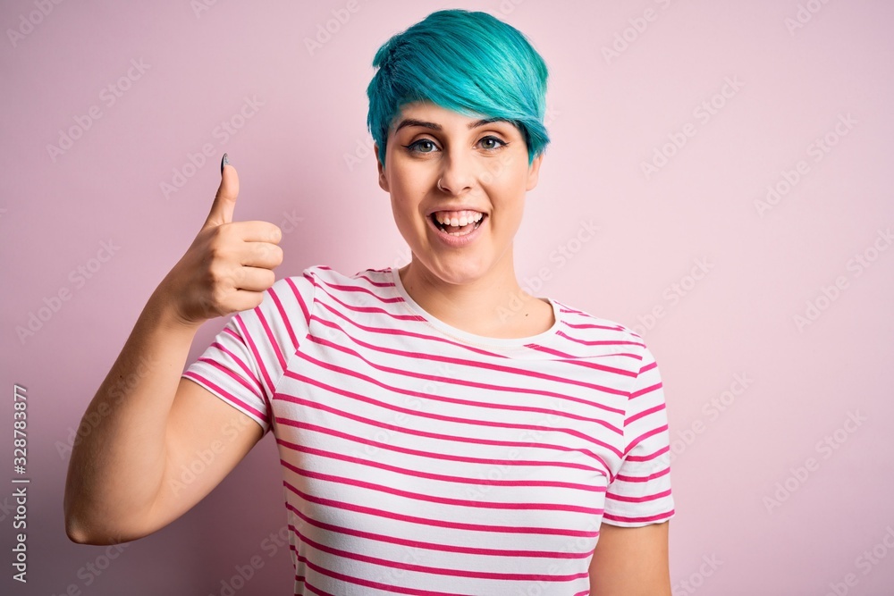 Young beautiful woman with blue fashion hair wearing casual striped t-shirt doing happy thumbs up gesture with hand. Approving expression looking at the camera showing success. Young beautiful woman with blue fashion hair wearing casual striped t-shirt doing happy thumbs up gesture with hand. Approving expression looking at the camera showing success.