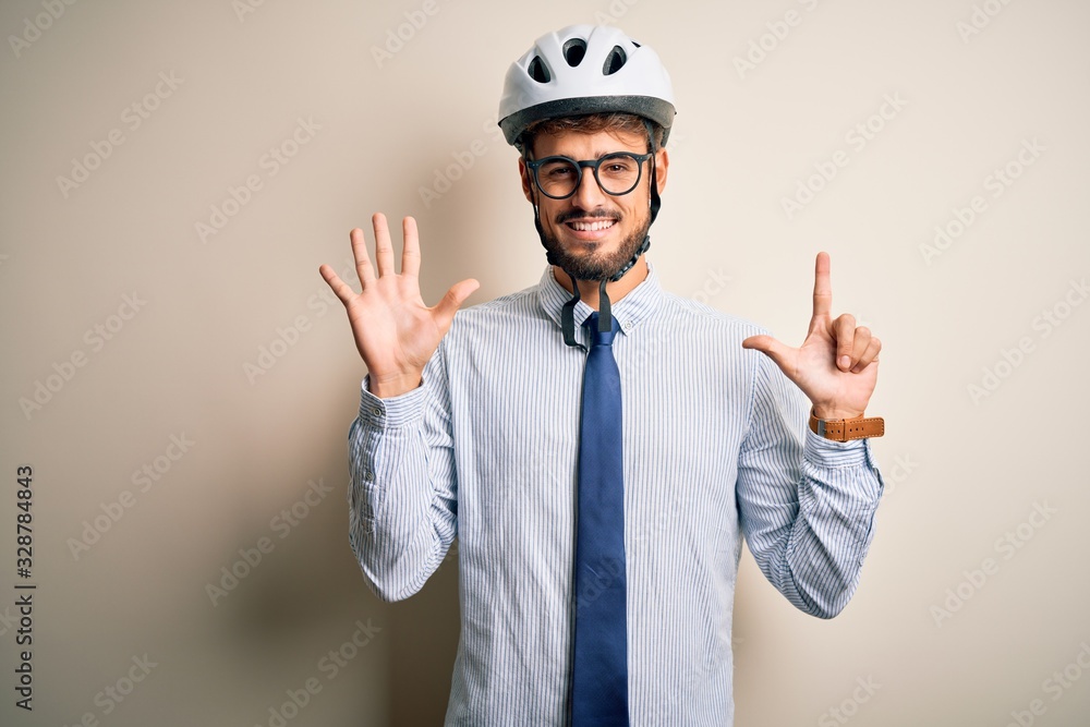 Young businessman wearing glasses and bike helmet standing over isolated white bakground showing and pointing up with fingers number seven while smiling confident and happy.