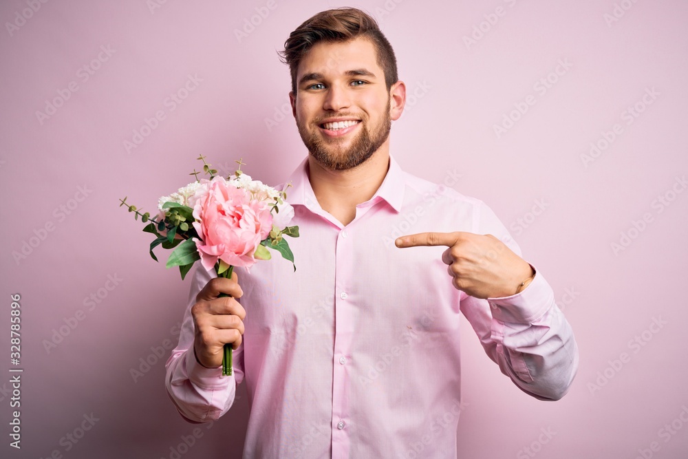 Young blond romantic man with beard and blue eyes holding beautiful bouquet of flowers very happy pointing with hand and finger Young blond romantic man with beard and blue eyes holding beautiful bouquet of flowers very happy pointing with hand and finger