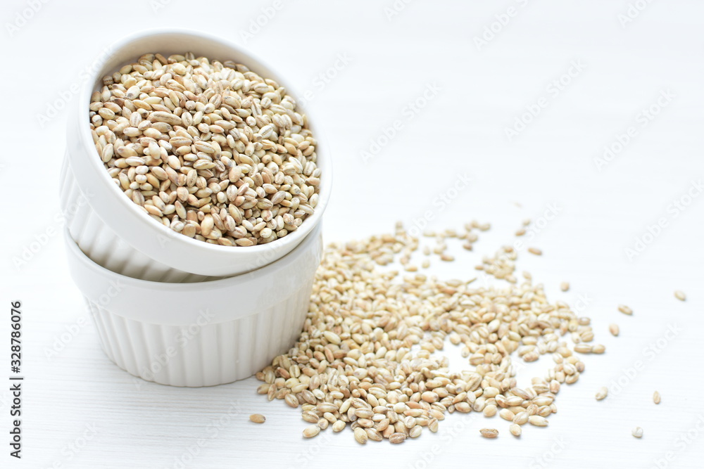 Raw barley grains, released in containers on white wooden background Raw barley grains, released in containers on white wooden background