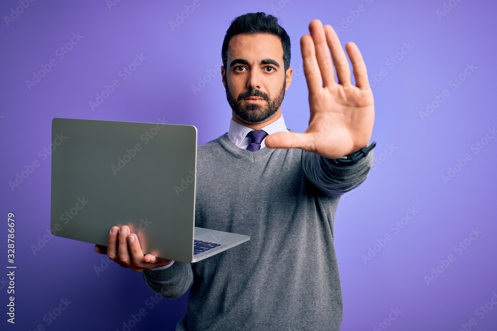 Young handsome businessman with beard working using laptop over purple background with open hand doing stop sign with serious and confident expression, defense gesture Young handsome businessman with beard working using laptop over purple background with open hand doing stop sign with serious and confident expression, defense gesture