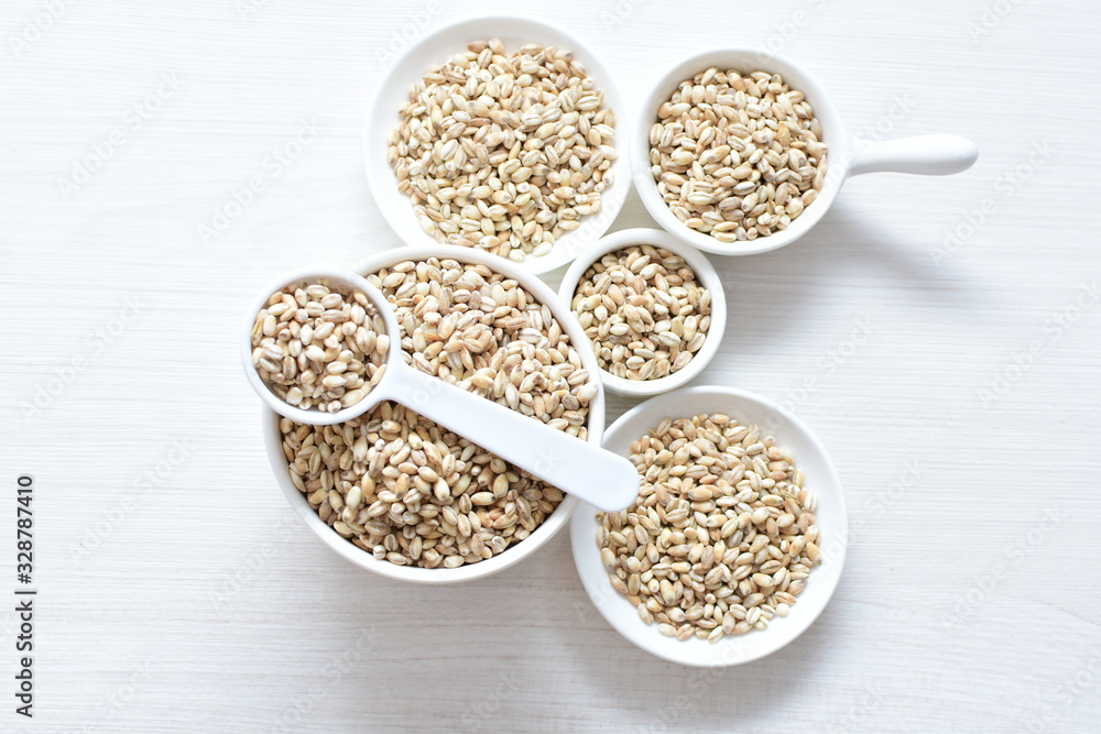 Raw barley grains, released in containers on white wooden background Raw barley grains, released in containers on white wooden background