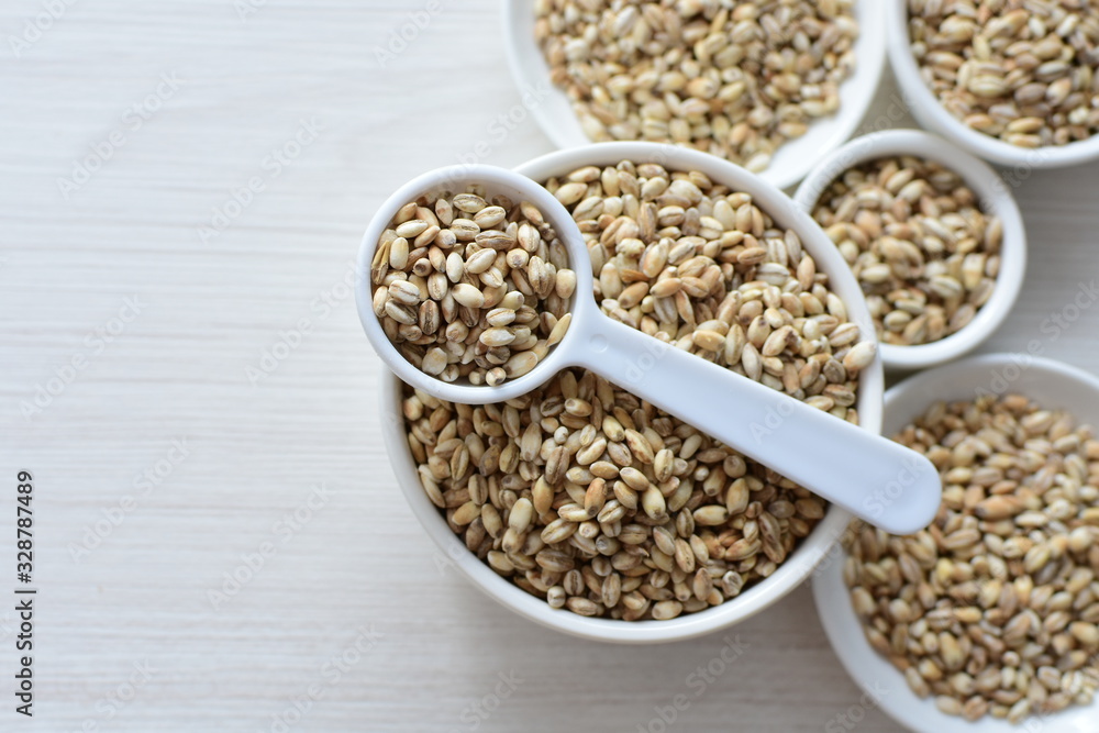 Raw barley grains, released in containers on white wooden background Raw barley grains, released in containers on white wooden background