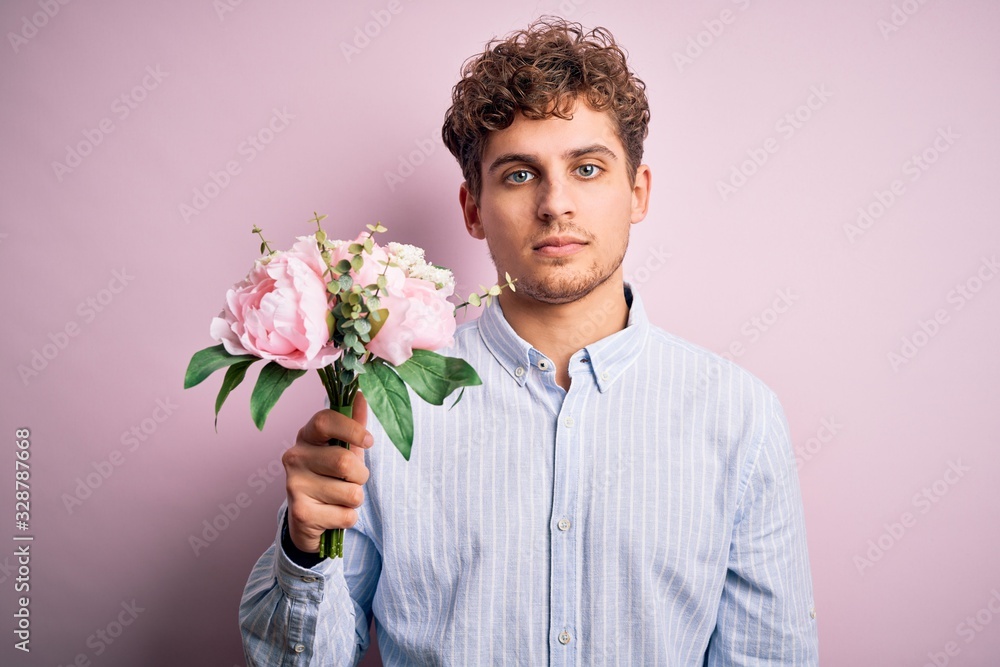 Young blond man with curly hair holding beautiful bouquet over isolated pink background with a confident expression on smart face thinking serious Young blond man with curly hair holding beautiful bouquet over isolated pink background with a confident expression on smart face thinking serious