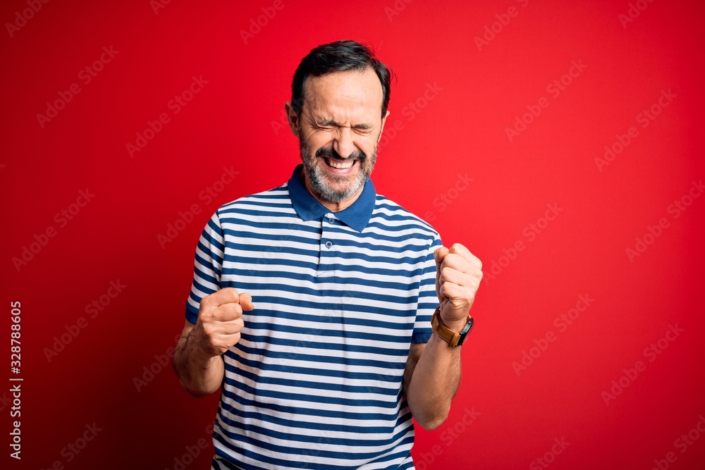 Middle age hoary man wearing casual striped polo standing over isolated red background excited for success with arms raised and eyes closed celebrating victory smiling. Winner concept. Middle age hoary man wearing casual striped polo standing over isolated red background excited for success with arms raised and eyes closed celebrating victory smiling. Winner concept.