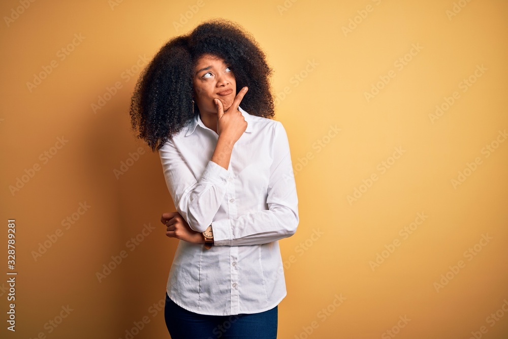 Young beautiful african american elegant woman with afro hair standing over yellow background Thinking worried about a question, concerned and nervous with hand on chin Young beautiful african american elegant woman with afro hair standing over yellow background Thinking worried about a question, concerned and nervous with hand on chin