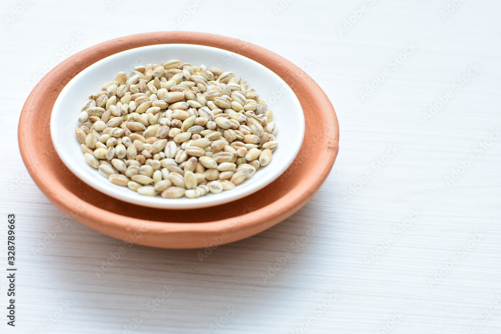Raw barley grains, released in containers on white wooden background Raw barley grains, released in containers on white wooden background