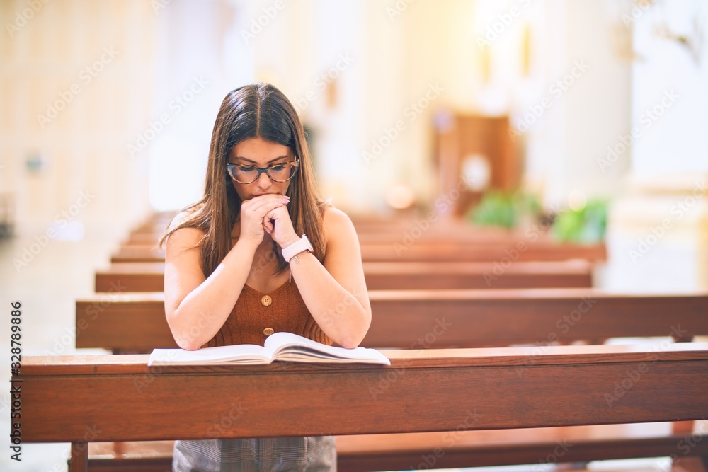 Young beautiful woman praying on her knees in a bench at church Young beautiful woman praying on her knees in a bench at church