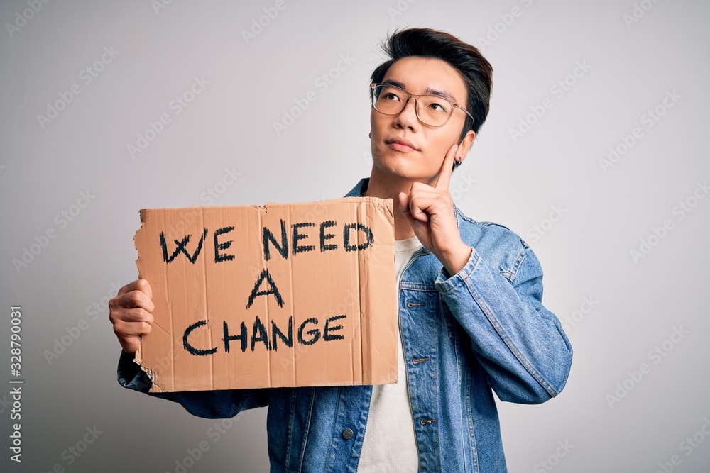 Young handsome chinese activist man protesting asking for change holding poster serious face thinking about question, very confused idea Young handsome chinese activist man protesting asking for change holding poster serious face thinking about question, very confused idea