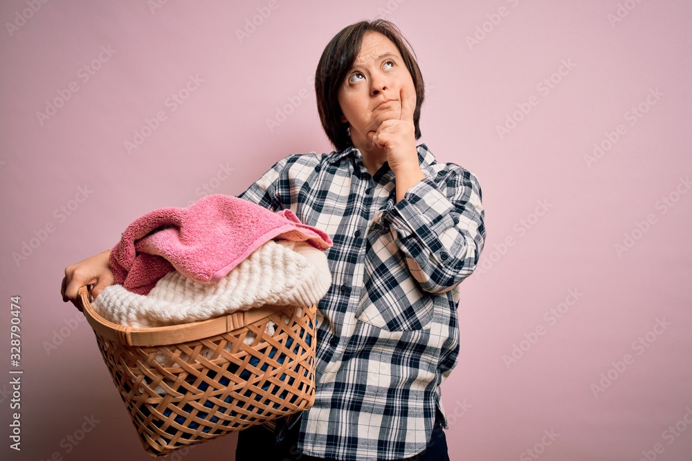 Young down syndrome woman doing housework domestic chores holding laundry wicker basket serious face thinking about question, very confused idea Young down syndrome woman doing housework domestic chores holding laundry wicker basket serious face thinking about question, very confused idea