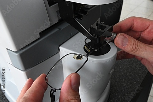 Optician hands adjusting eyeglasses during measurement of dioptry with modern digital lens meter.  photo