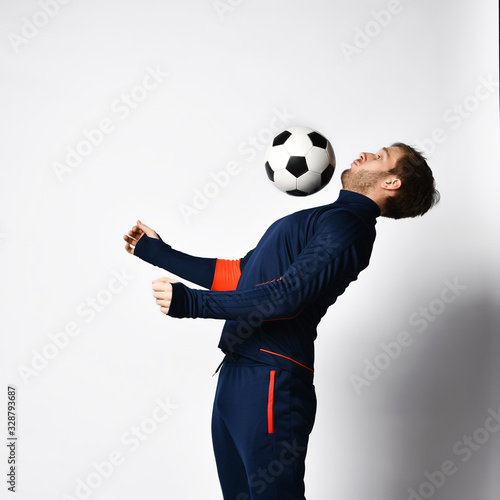 Professional soccer player in blue tracksuit is performing tricks with ball, posing sideways isolated on white. Close up