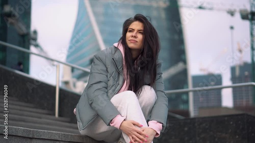 girl in tracksuit background buildings sits steps straightens her hair photo