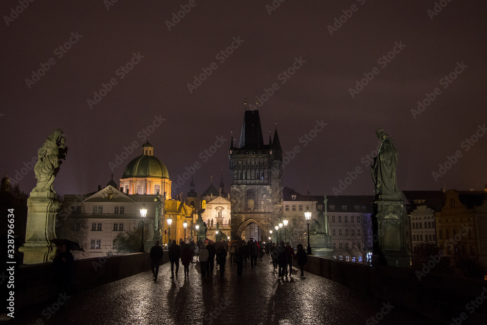 Fototapeta premium Old town bridge tower of Charles Bridge (Karluv Most), or staromestska mostecka vez in Prague, Czech Republic, at night, with the shapes of tourists walking on it
