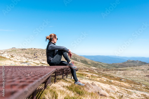 Sporty young female hiker taking a break sitting on the rusty steel boardwalk near the summit of Mount Kosciuszko (2228m above sea level) Kosciuszko National Park, New South Wales, Australia. photo