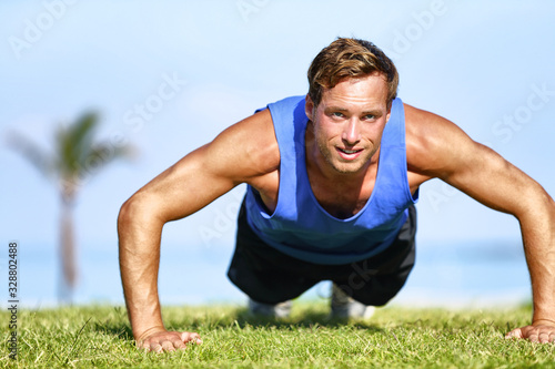 Fit man doing push-ups exercises strength training outdoor on beach park gym. Workout healthy active lifestyle.