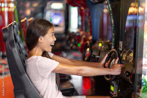 Arcade game machine adult woman having fun playing racing car videogame driving virtual sports cars.