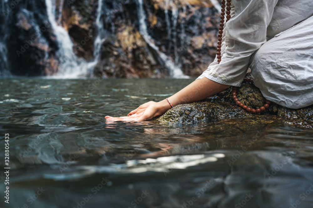 Close hand of a woman in white clothes by a waterfall