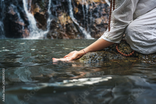 Close hand of a woman in white clothes by a waterfall