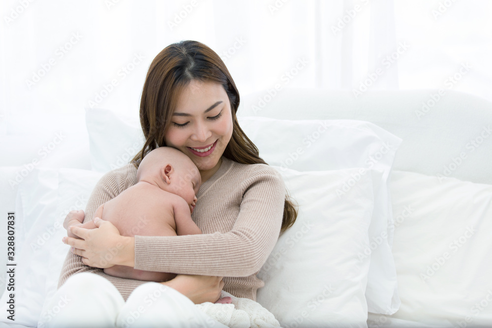 Beautiful mom supports and tenderly cuddles the newborn baby gently while the infant is sleeping on the chest. Asian mother looking at the baby with love and showing protection. Beautiful mom supports and tenderly cuddles the newborn baby gently while the infant is sleeping on the chest. Asian mother looking at the baby with love and showing protection.