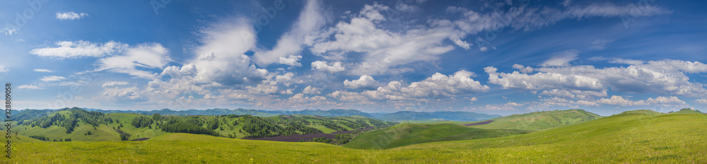 Panoramic view of green hills and picturesque blue sky with white clouds. Spring greens of meadows and forests. Countryside in the mountains of Altay.