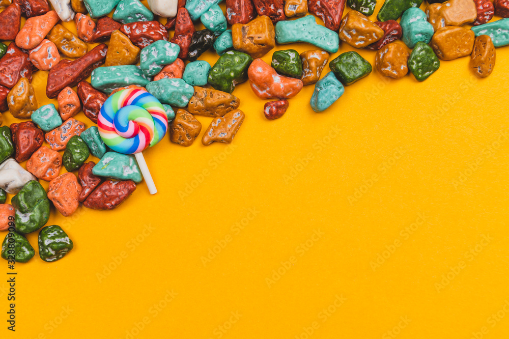 Lollipop and candy pebbles on a yellow background. sweets in the form of colored stones. colorful candies
