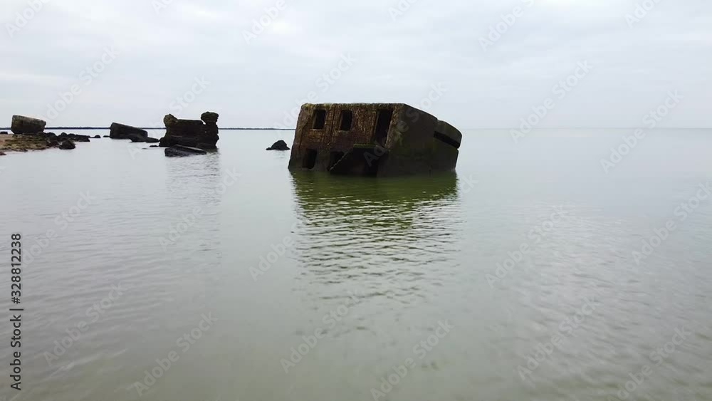 Aerial view of abandoned seaside fortification bunker in water at Karosta Northern Forts on the beach of Baltic sea in Liepaja in overcast spring day, low altitude ascending drone shot moving forward Aerial view of abandoned seaside fortification bunker in water at Karosta Northern Forts on the beach of Baltic sea in Liepaja in overcast spring day, low altitude ascending drone shot moving forward