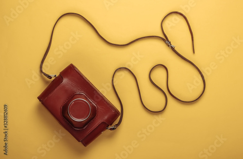 Retro camera in a leather case with strap on yellow pastel background. Top view