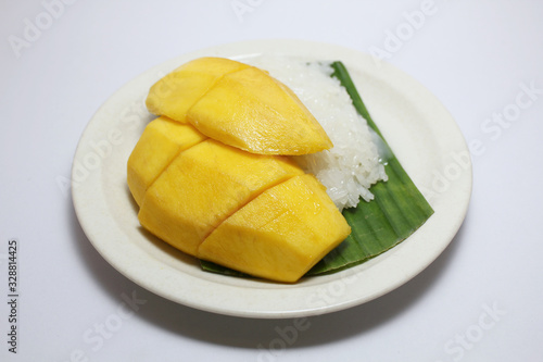 Most popular Thai dessert, ripe yellow mango with sticky rice served with coconut milk on banana leaf on white plate