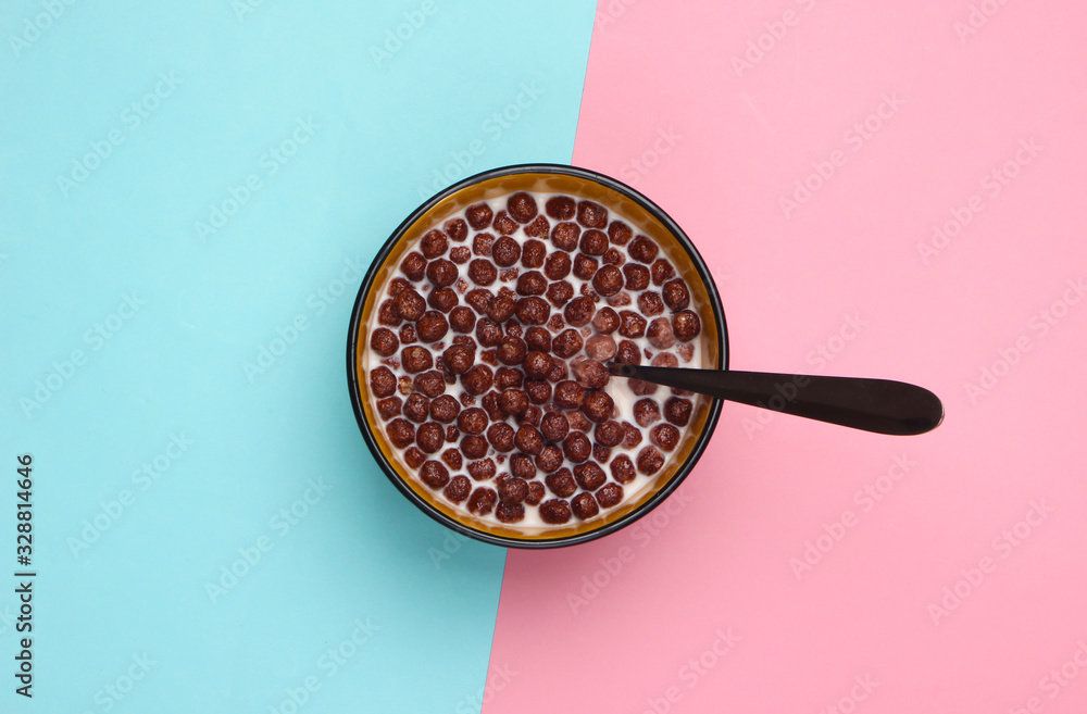 Chocolate cereal balls with milk and spoon in bowl on pink blue pastel background. Concept for a healthy diet. Top view Chocolate cereal balls with milk and spoon in bowl on pink blue pastel background. Concept for a healthy diet. Top view