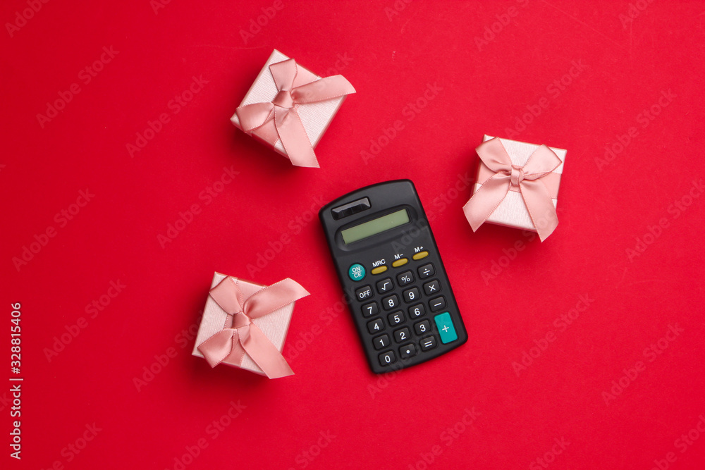 Calculating the value of the gift. Gift boxes and calculator on a red background. Top view Calculating the value of the gift. Gift boxes and calculator on a red background. Top view