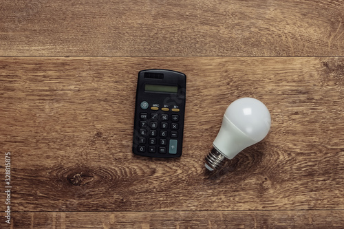 Calculator and light bulb on a wooden floor. Economy, eco concept. Save your money. Top view