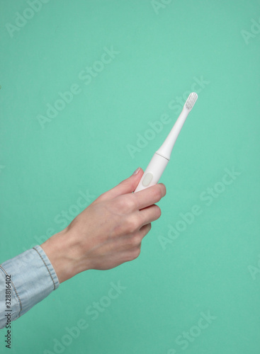 Female hand holds a modern electro toothbrush on a blue background