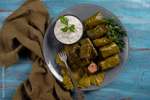 Traditional Georgian dolma in grape leaves on a wooden table with sour cream sauce. photo