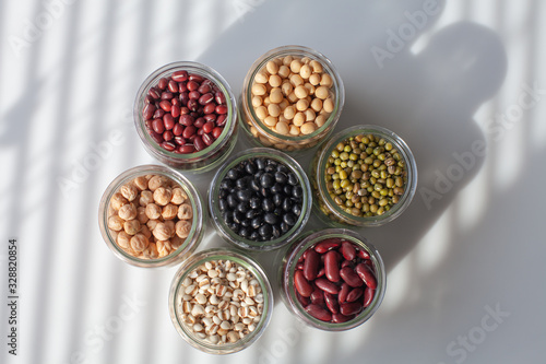 Seven jars, each containing one type of beans. Natural ingredients of cooking. Top shot shows a dramatic pattern of circles on white background. Natural lights shedding on the elements.