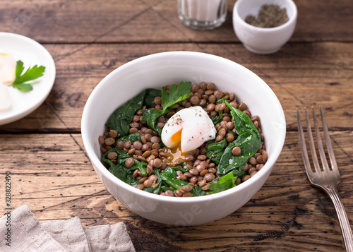 Boiled lentils with spinach  herbs  spices and poached egg in ceramic bowls on a wooden background. Simple healthy homemade food 