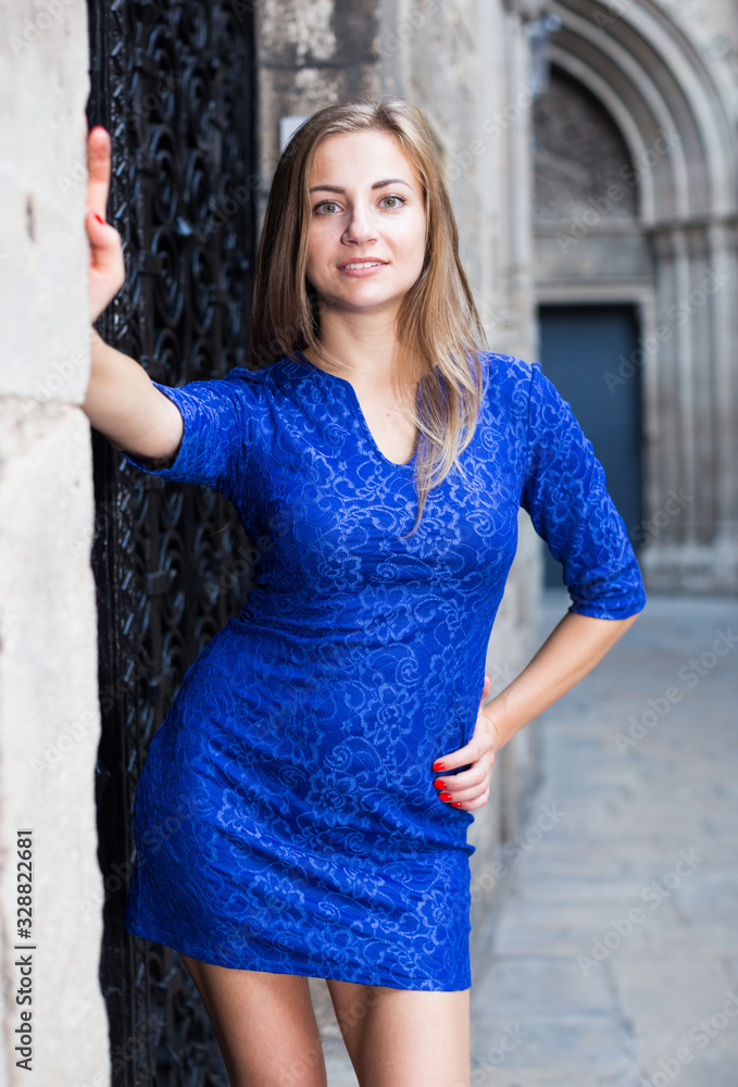 Cheerful female is playfully posing in blue dress near black door