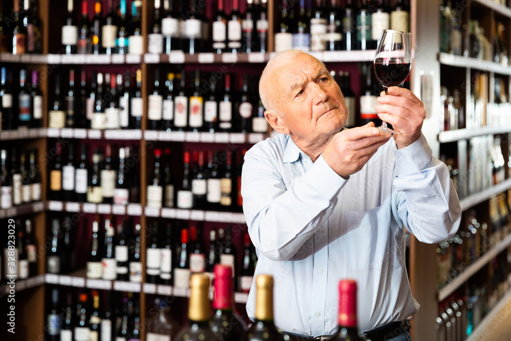 Elderly man checks the color and taste of red wine in a liquor store