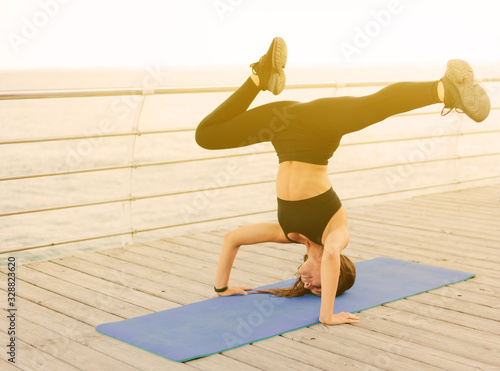 Young fitness woman doing yoga exercises standing on her head on a gymnastic mat at the beach